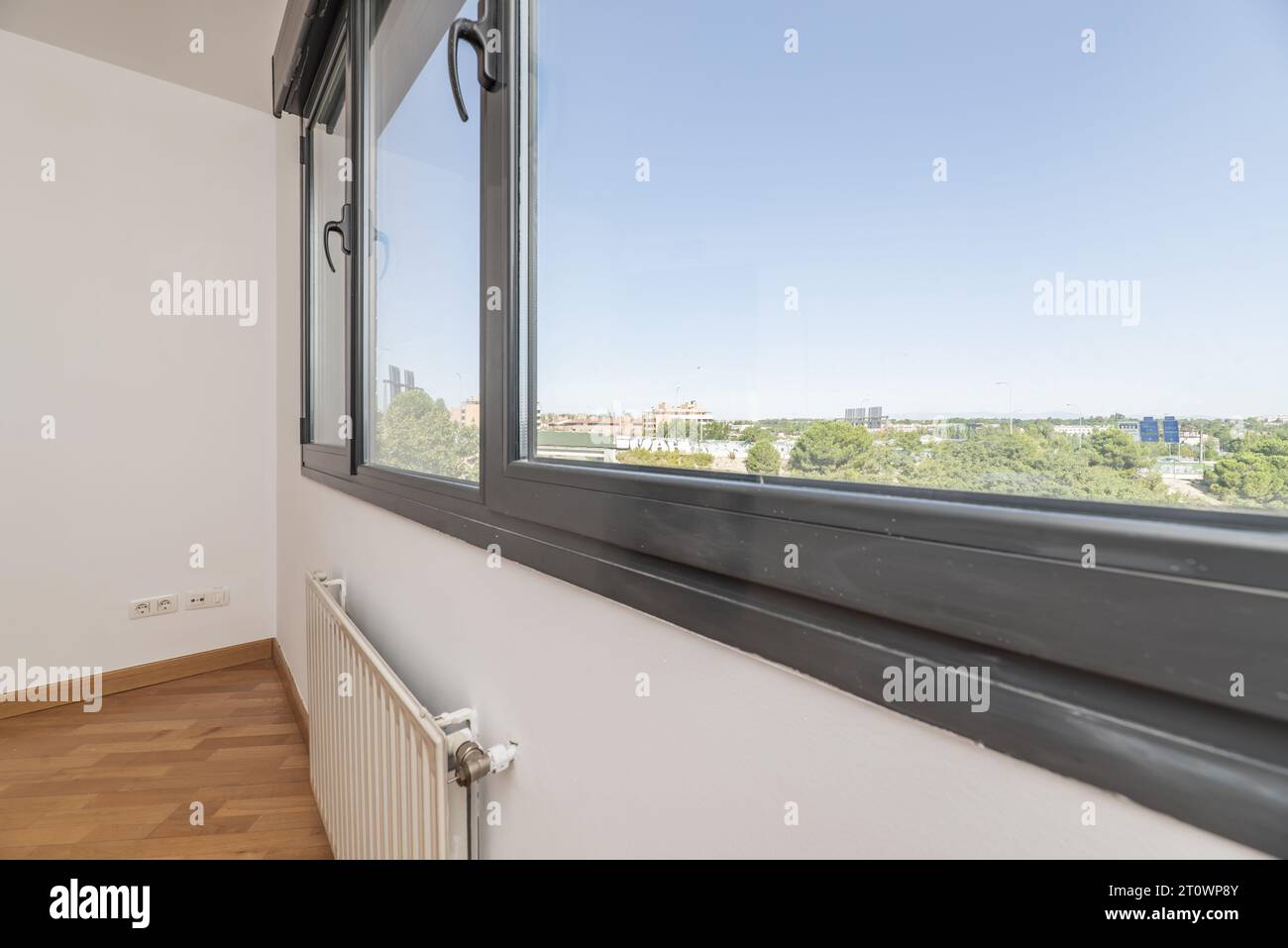 A gray aluminum window overlooking an urban park with trees in a room with white walls Stock Photo