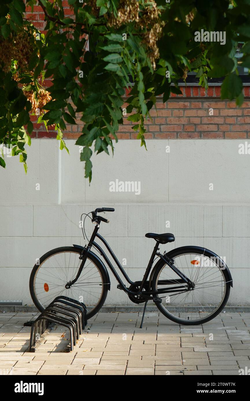 Black retro bicycle parked on bike rack in front of brick wall in Bucharest Stock Photo
