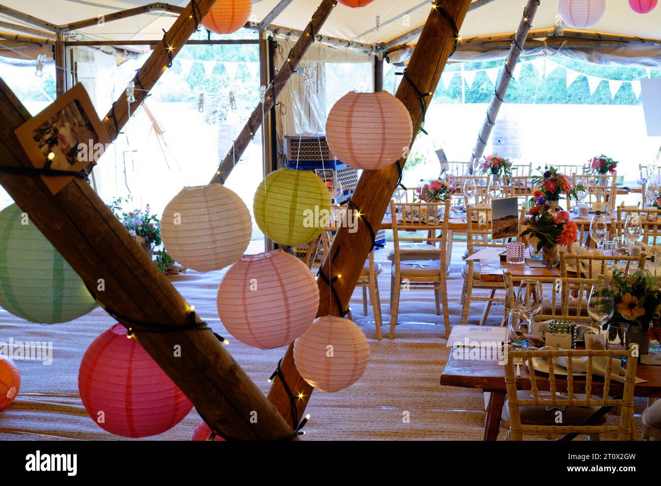 Wedding marquee decorated and ready for the guests to arrive. Tables, chairs, flowers and place settings. A rustic teepee design of tent. Stock Photo