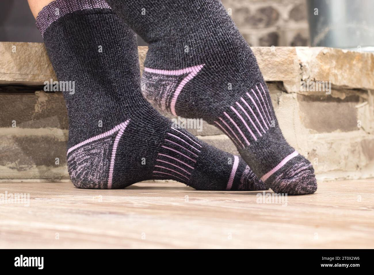 Pointed toe on feet with warm grey and pink socks in front of a stone wall. Stock Photo