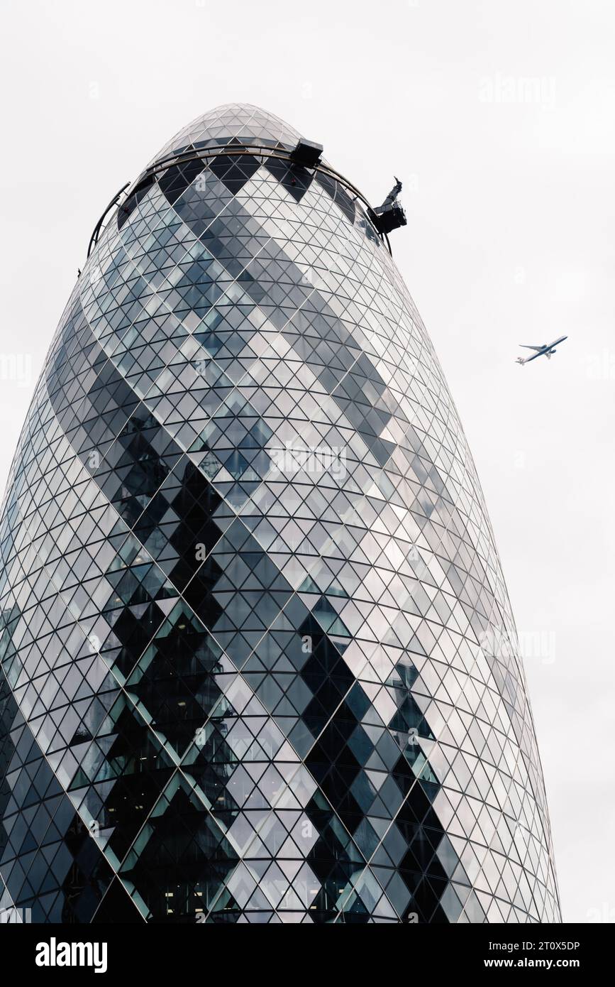 London, UK - August 25, 2023: The Gherkin Building or 30 St Mary Axe by Norman Foster architects. City of London. Plane flying on background Stock Photo