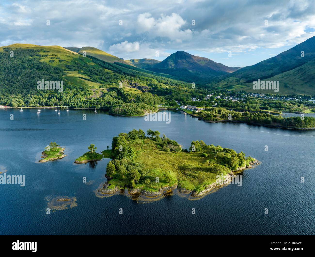 Aerial view of the island of Eilean Munde, behind it the village of Ballachulish with the harbour and the former slate quarry at the western part of Stock Photo