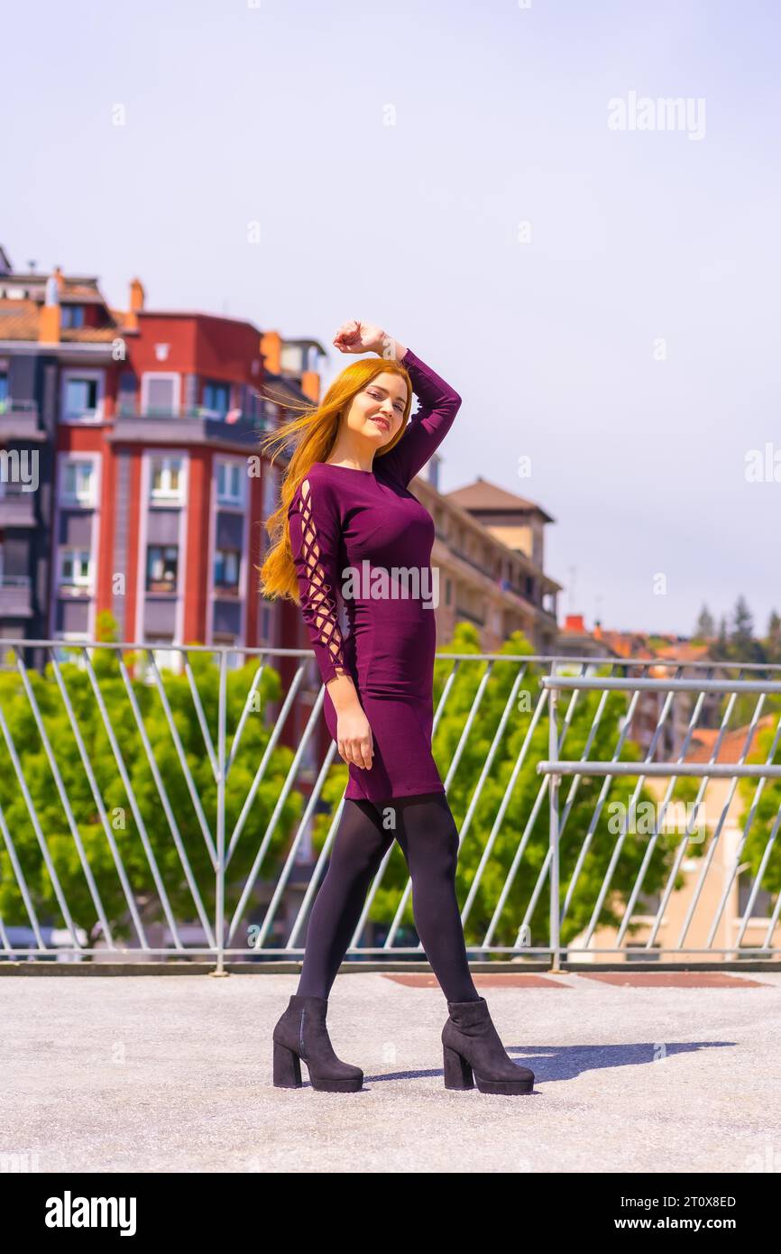 Beautiful woman in purple dress and black boots enjoying in a park in the city, posing looking at camera Stock Photo