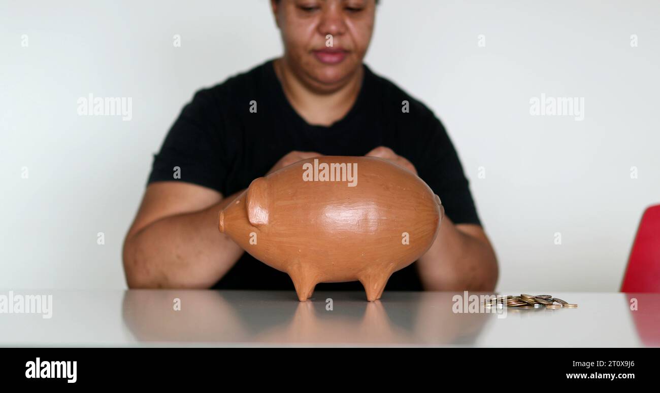 African woman inserting coins inside piggy bank Stock Photo - Alamy
