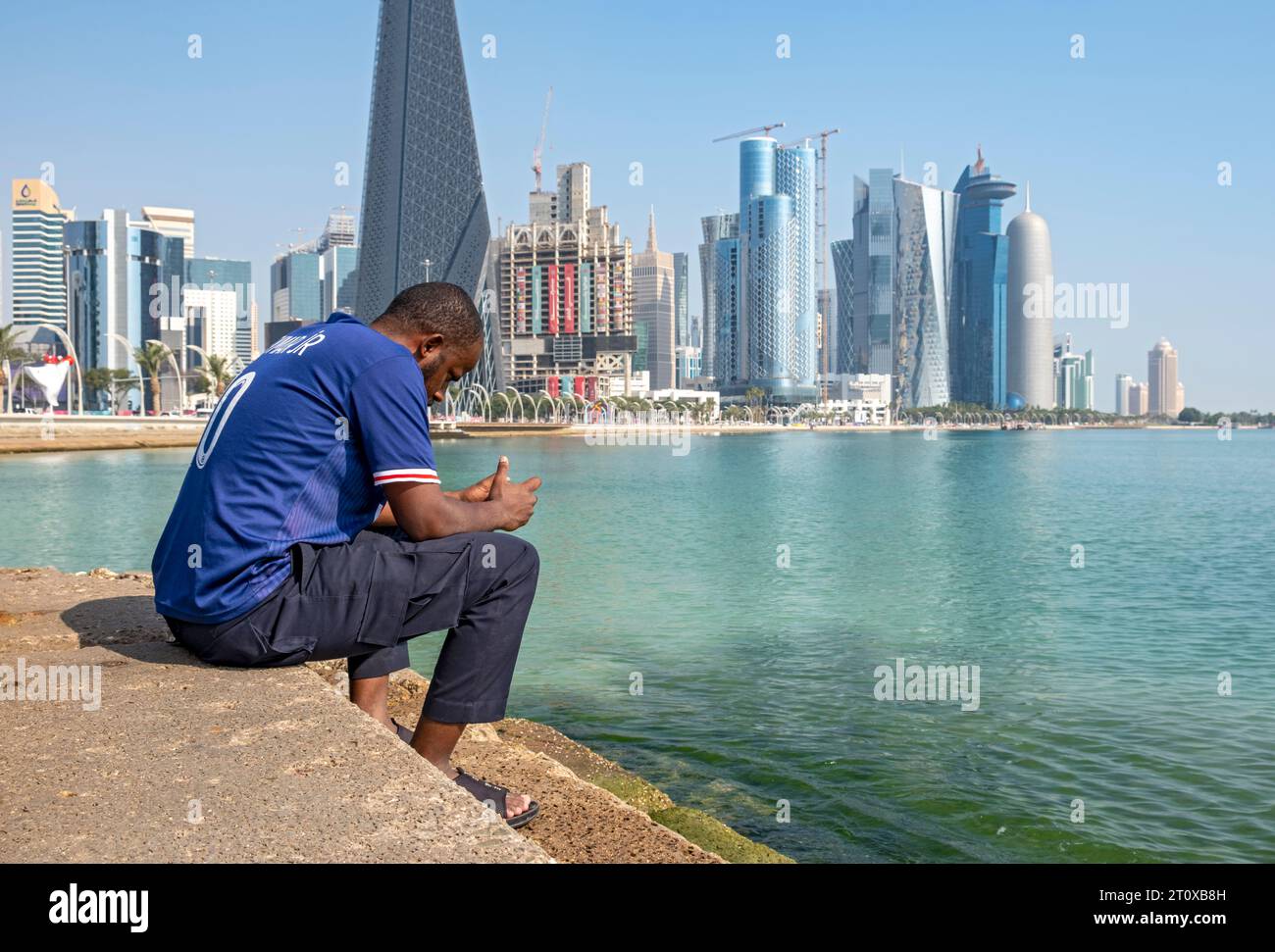 Man sits on steps of Corniche with skyscrapers in background, West Bay, Doha, Qatar Stock Photo