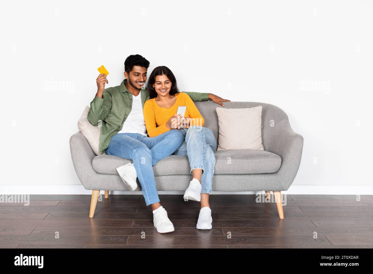 Indian couple sitting on sofa using cellphone and credit card Stock Photo