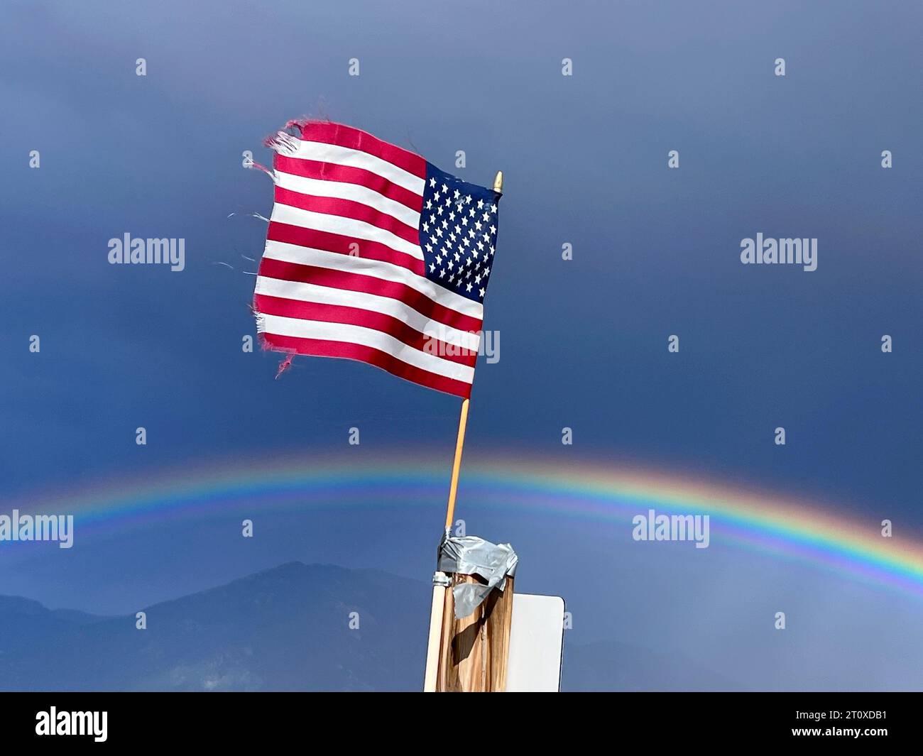 A tattered American flys against a perfect rainbow Stock Photo