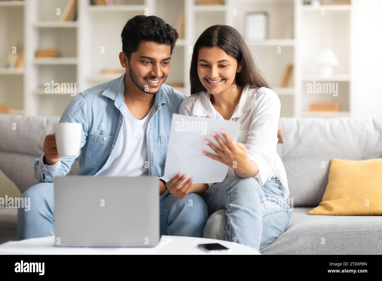 Happy indian couple attentively checking documents and using laptop Stock Photo