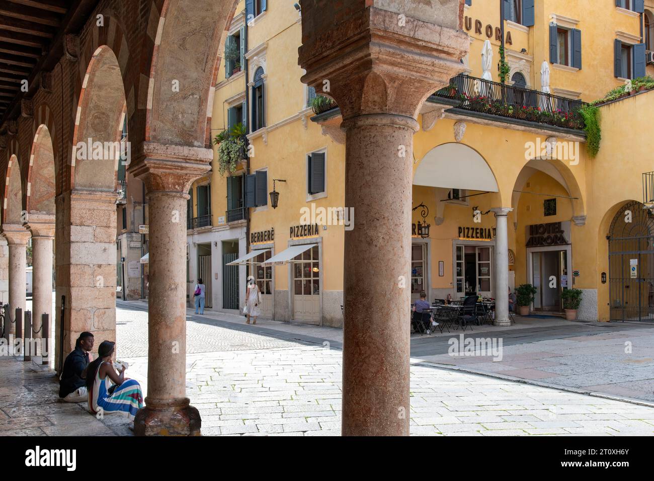 Verona, Italy-June 12, 2023; View of tourist sitting on steps under the arches of the medieval edifice Domus Mercatorum or Casa dei Mercanti on Piazza Stock Photo