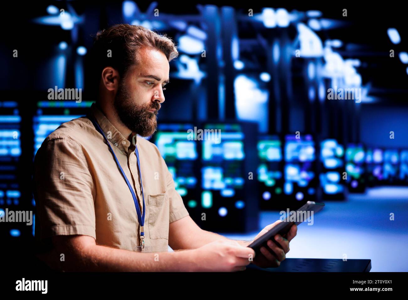 Skilled mechanic resolving performance related issues in server room. Expert utilizing tablet to identify operational problems causing high tech facility electronics slowdown Stock Photo
