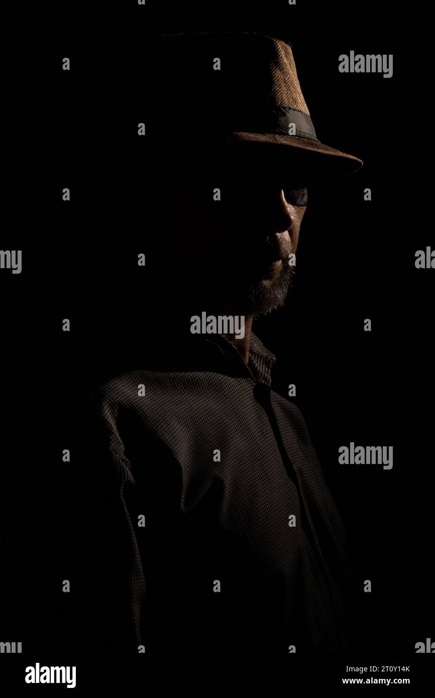 Discreet portrait of detective man with hat in darkness. Dark room art. Stock Photo