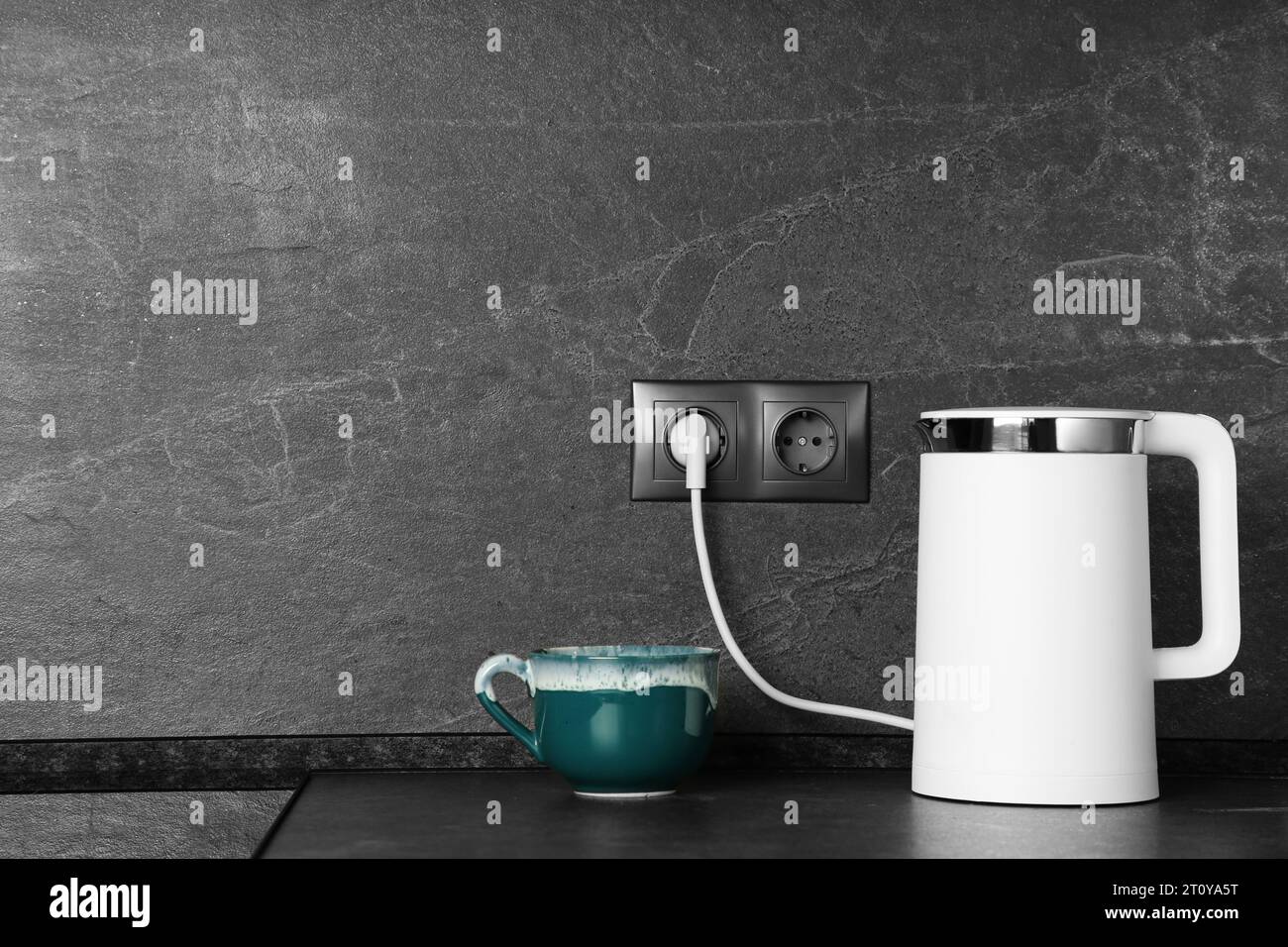 Electric kettle plugged into power socket on dark grey wall indoors
