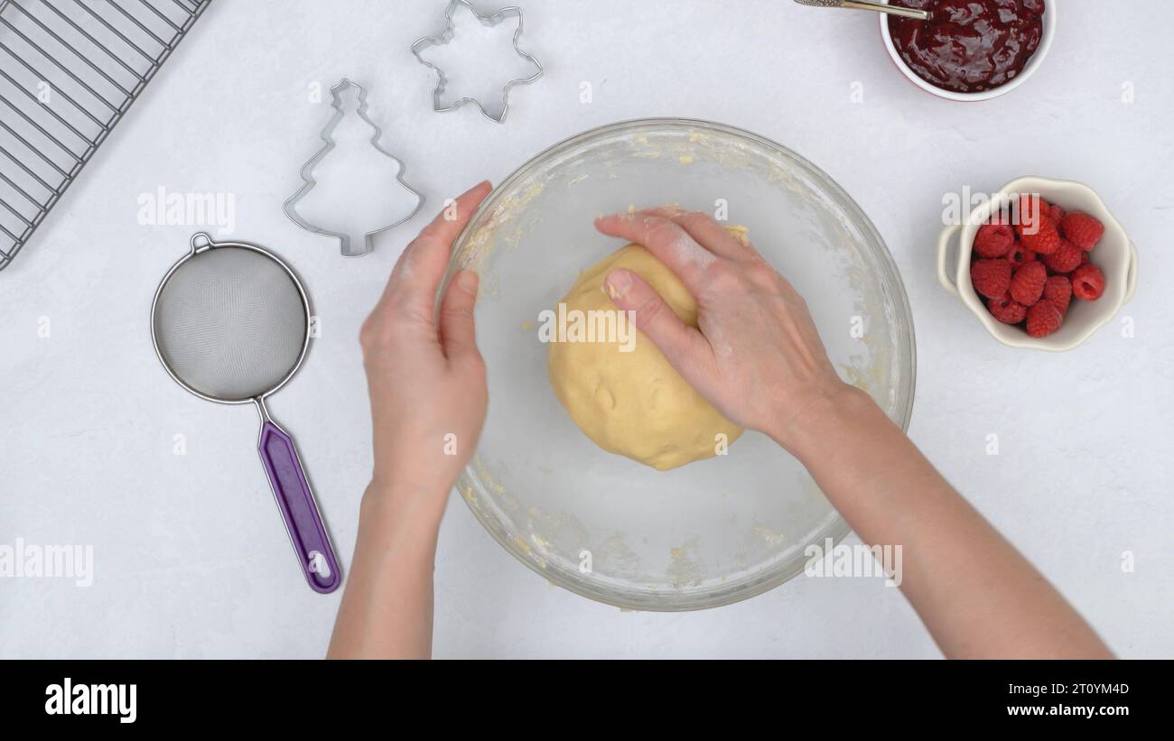 Cookie dough in a glass bowl. Chef shaping the dough into a disk. Christmas shortbread cookies with raspberry preserves recipe. Stock Photo