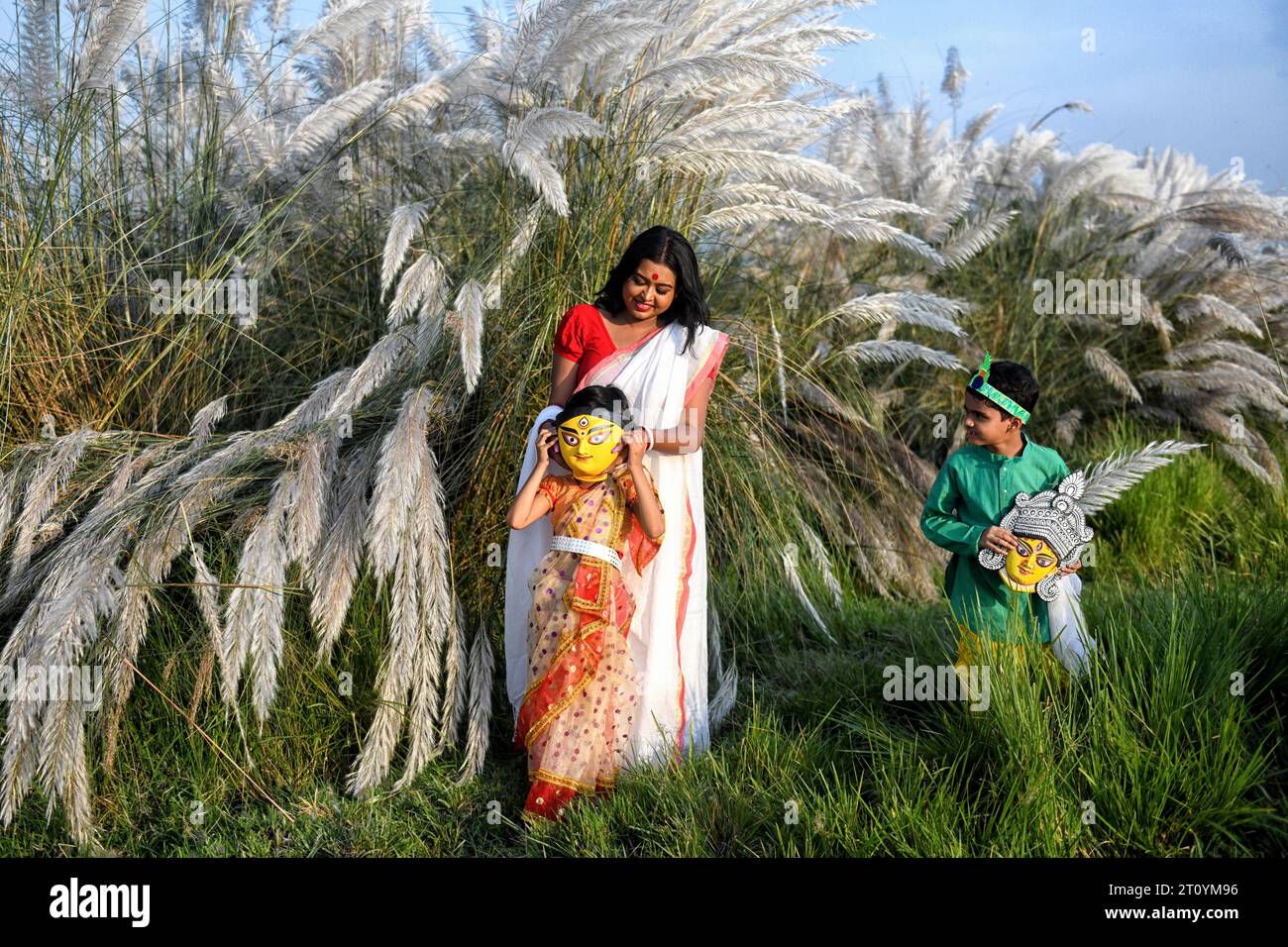 Fashion Model Rima Bhattacharya and two little kids name Aradhya & Kiaan pose for a photo with a Clay face of Durga idol during the Agomoni Concept outdoor Photo shoot in a Catkins or Kashful filled area around 60km from Kolkata. Fashion Model Rima Bhattacharya poses for a photo for the Photo Series based on Theme of Durga Puja vibes in India. Rima Bhattacharya, a Fashion Model and celebrity in the Bengali Fashion and television industry is collaborating with the Photo Series in promoting Durga Puja. The Photo Series is organized by a group of photographers aiming to document and promote the p Stock Photo