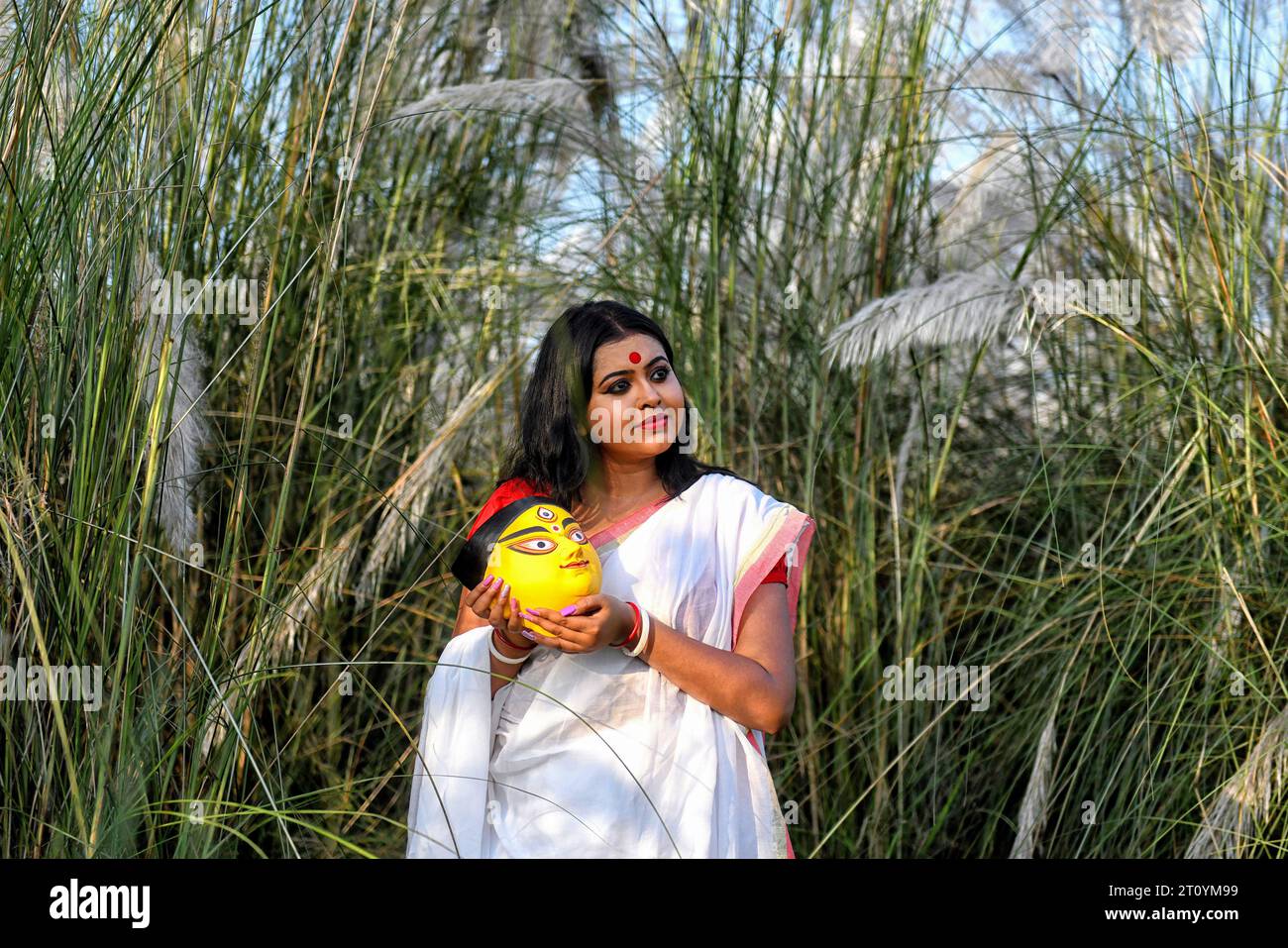 Fashion model, Rima Bhattacharya poses while wearing a traditional Indian saree and holding a Clay face of Durga idol during the Agomoni Concept outdoor Photo shoot in a Catkins or Kashful filled area around 60km from Kolkata. Fashion Model Rima Bhattacharya poses for a photo for the Photo Series based on Theme of Durga Puja vibes in India. Rima Bhattacharya, a Fashion Model and celebrity in the Bengali Fashion and television industry is collaborating with the Photo Series in promoting Durga Puja. The Photo Series is organized by a group of photographers aiming to document and promote the pre- Stock Photo