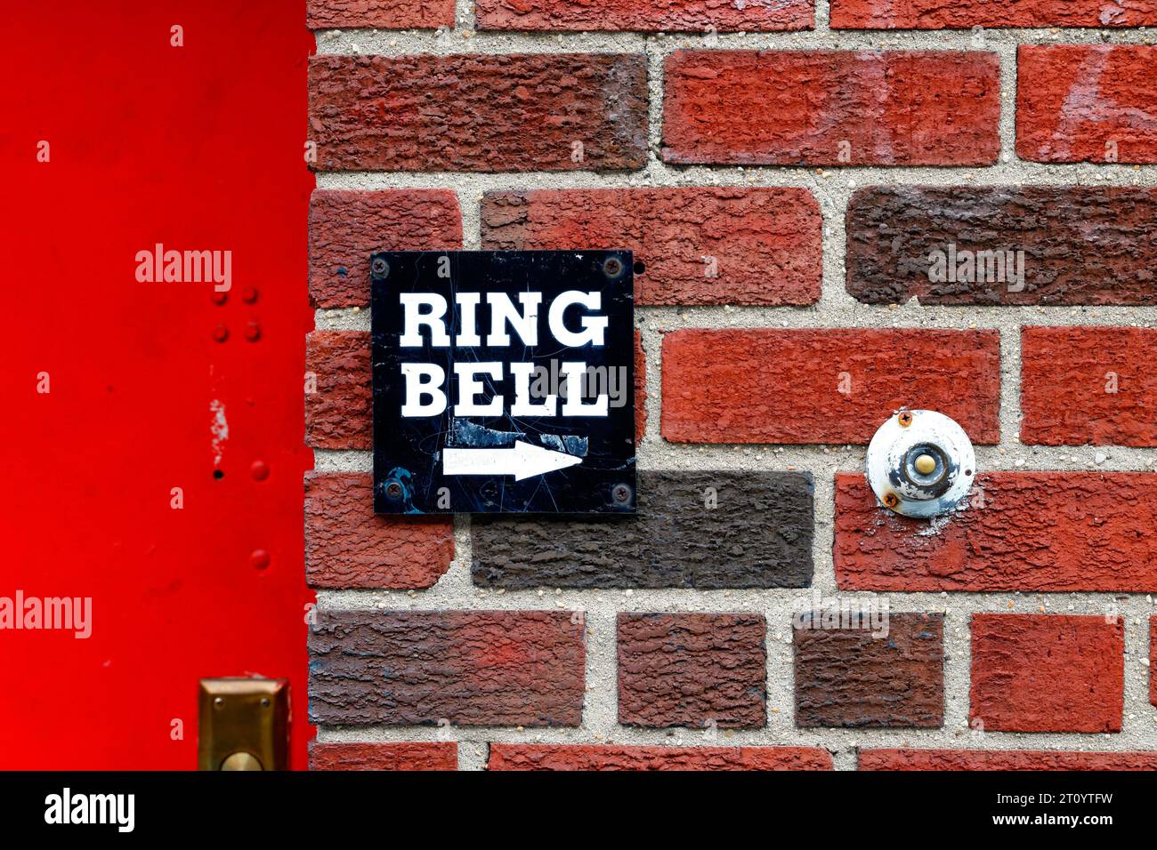 A Ring Bell sign next to a round door bell on a red brick wall Stock Photo