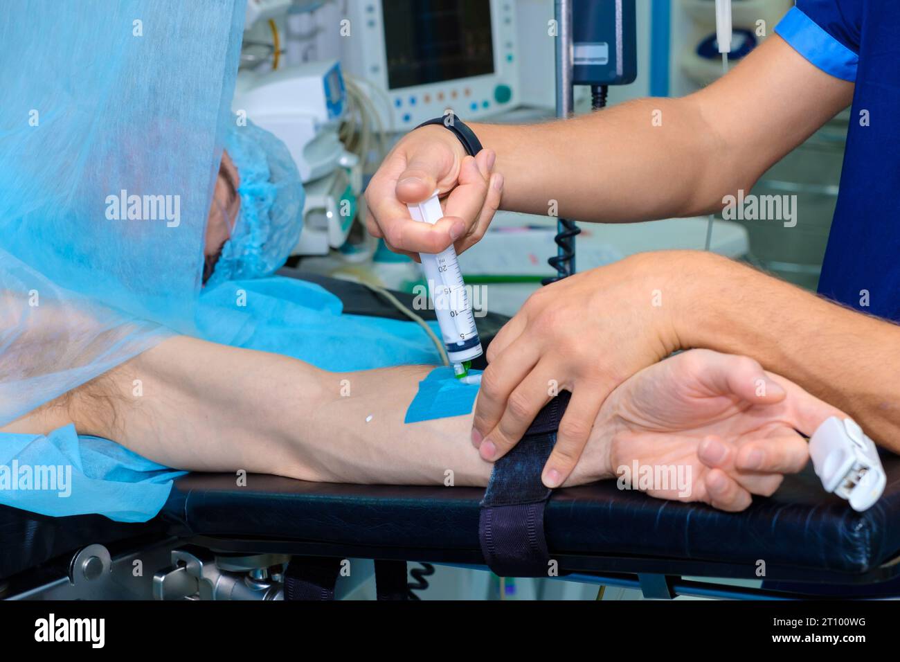 An anesthesiologist injects intravenous anesthesia with a large syringe into the patient's arm on the operating table. Surgery with general anesthesia. Stock Photo