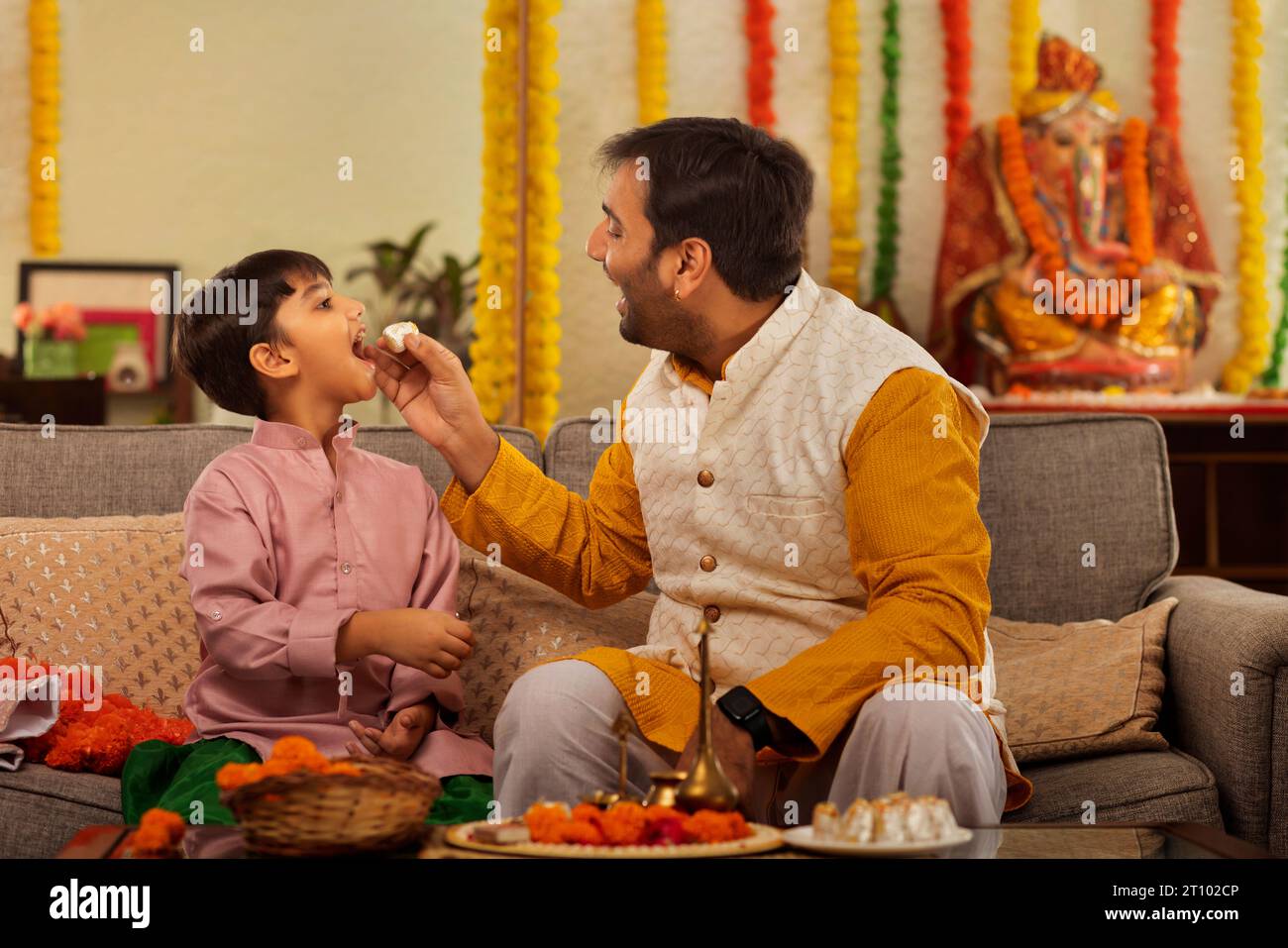 Father feeding modak to his son on the occasion of Ganesh Chaturthi Stock Photo