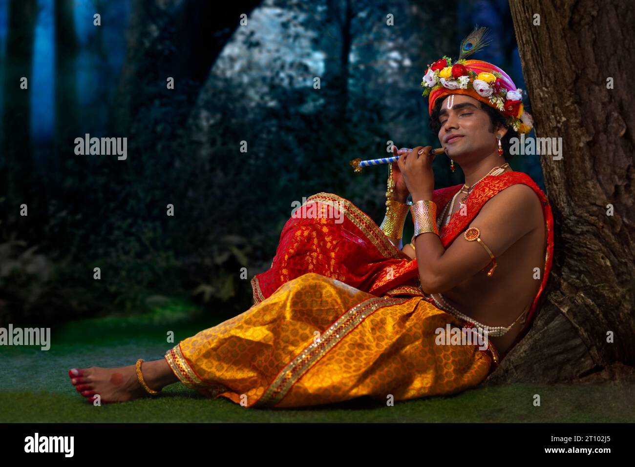 Young man dressed up as Lord Krishna and playing flute on the occasion of Janmashtami Stock Photo