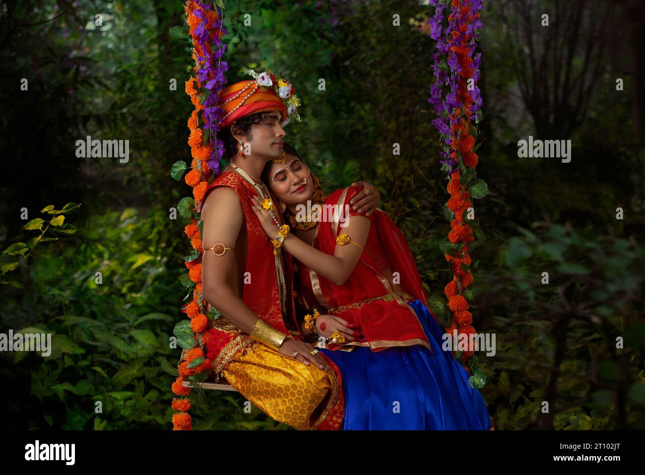 Young man and woman dressed up as Radha and Krishna and sitting together on a swing on the occasion of Janmashtami Stock Photo