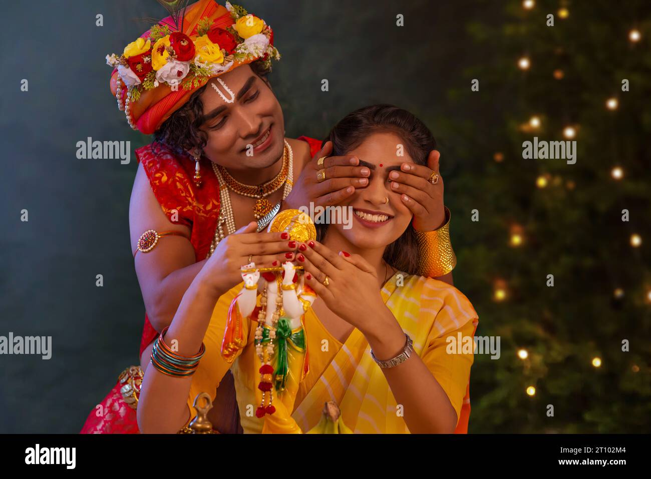 Young man dressed up as Lord Krishna and covering eyes of woman on the occasion of Janmashtami Stock Photo