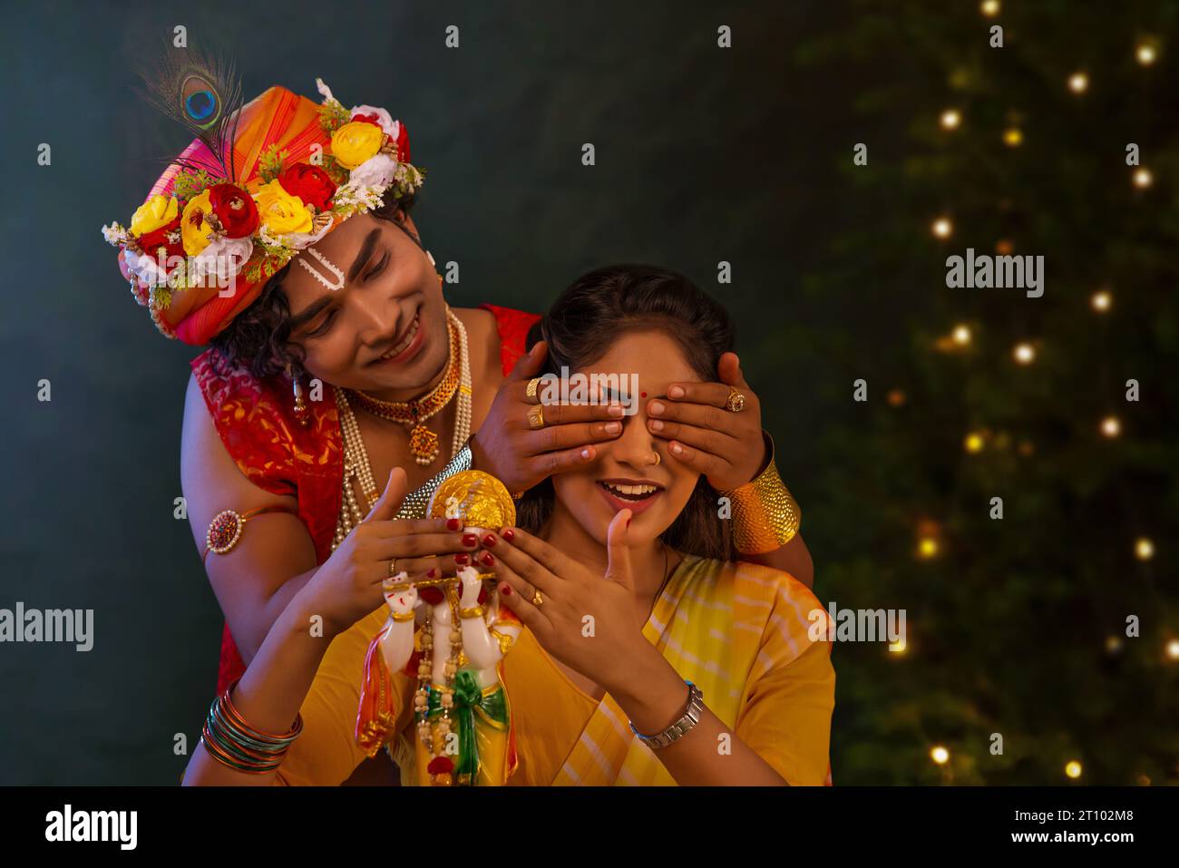 Young man dressed up as Lord Krishna and covering eyes of woman on the
