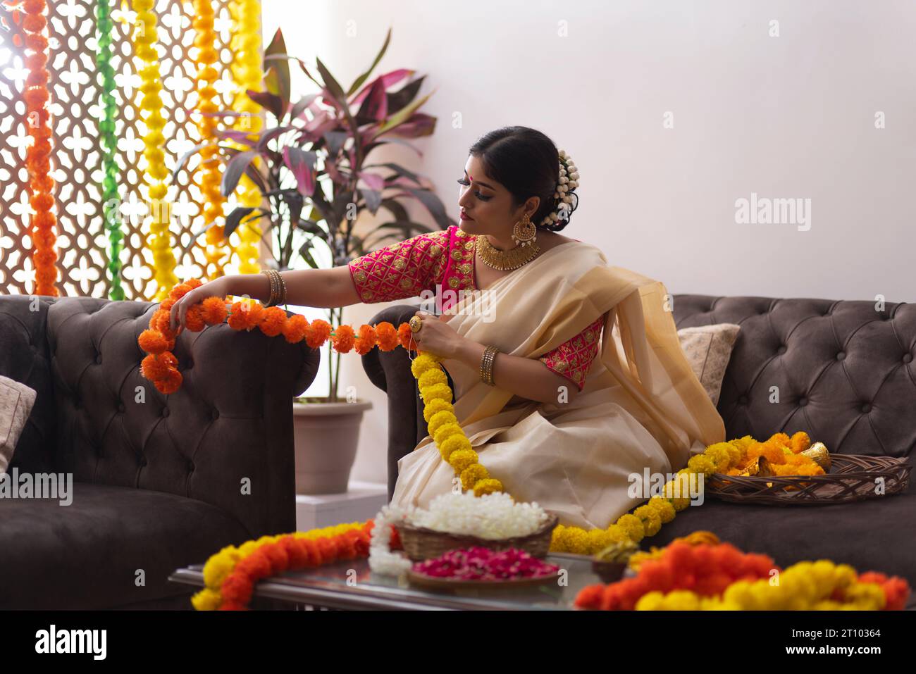 South Indian Woman in white saree garlanding flowers to celebrate Onam Stock Photo