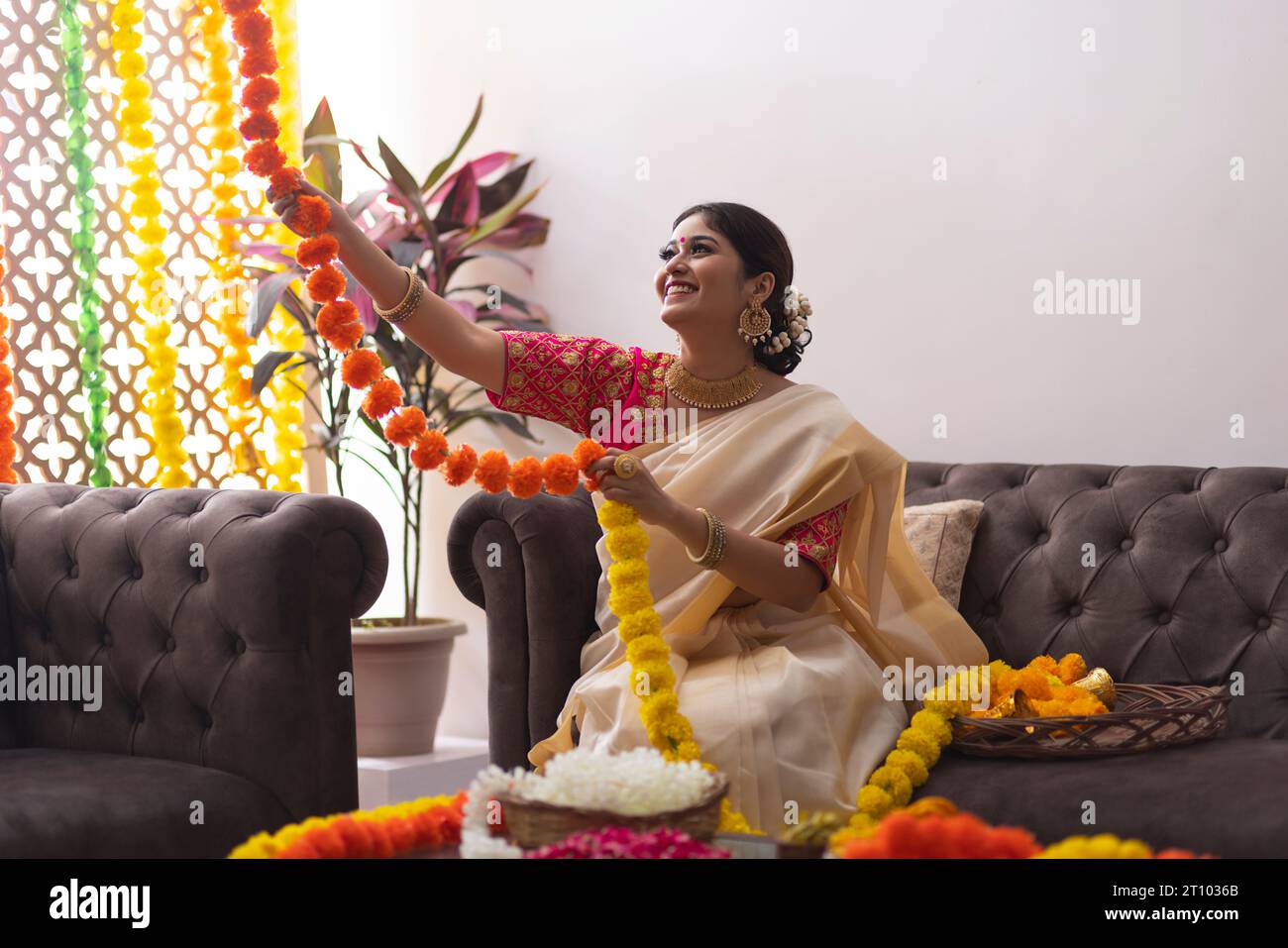 Woman in white saree decorating house with flower garland to celebrate Onam Stock Photo