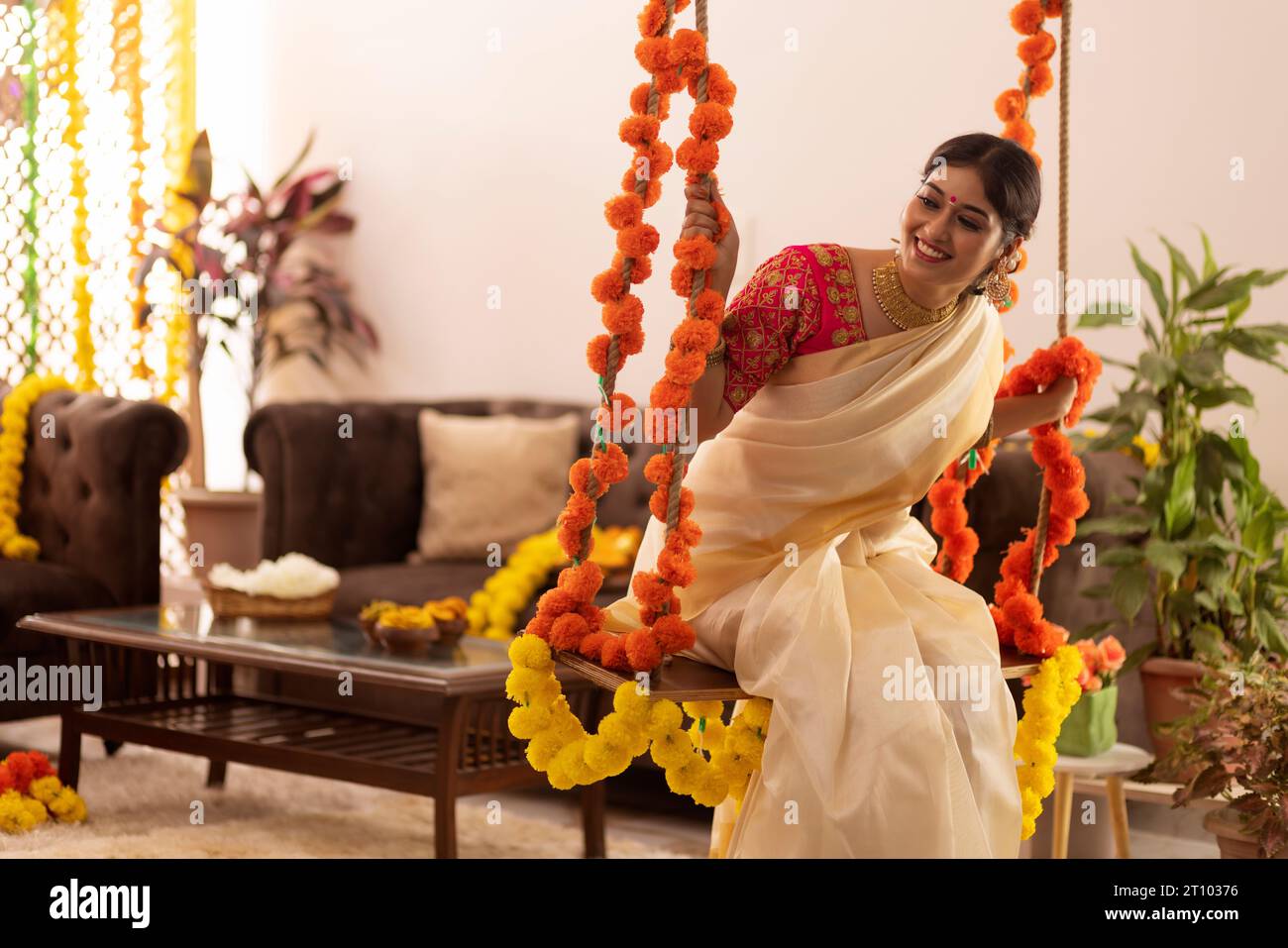 Woman in traditional clothing sitting on a swing decorated with flowers on Onam Stock Photo
