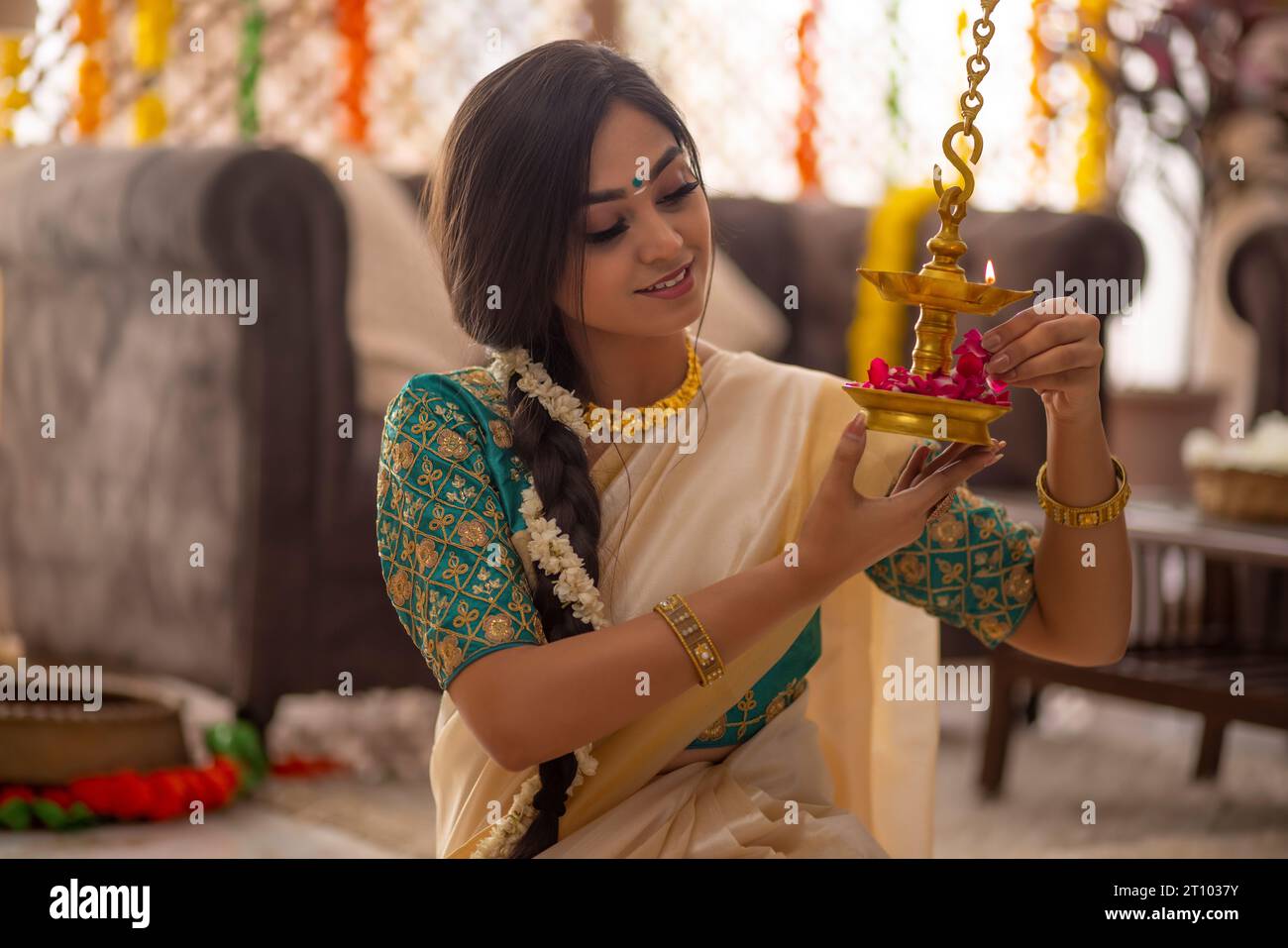 Woman in traditional clothing decorating diya with rose petals on Onam Stock Photo