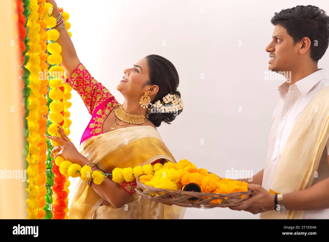 South Indian couple decorating house with flower garland to celebrate Onam Stock Photo