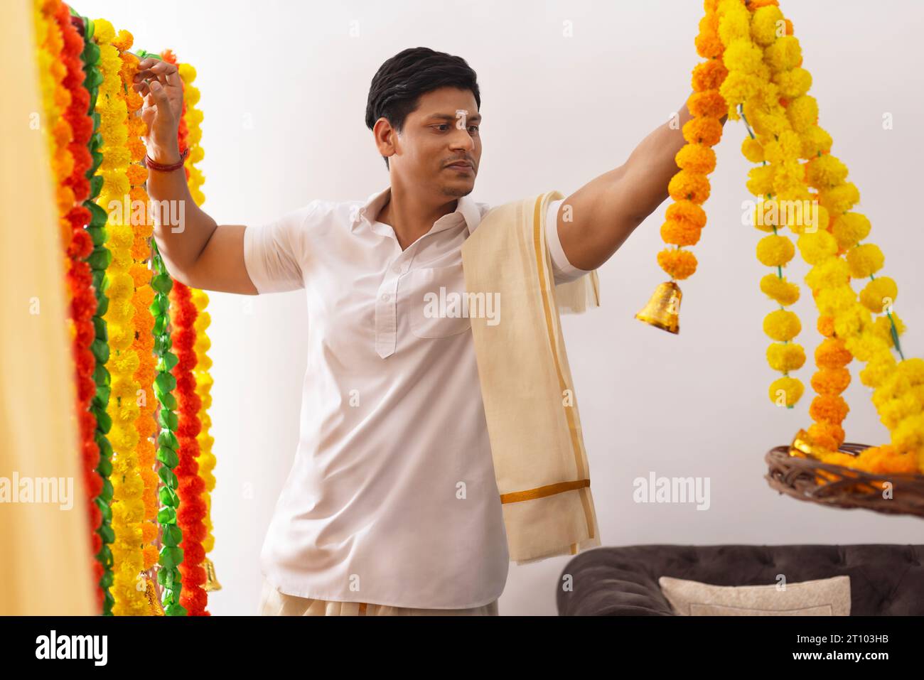 South Indian man decorating house with flower garland to celebrate Onam Stock Photo