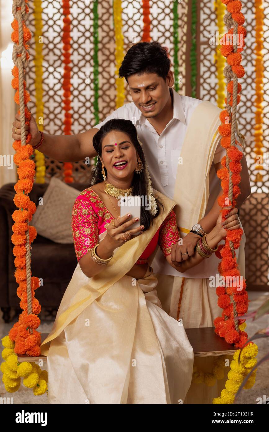South Indian couple using mobile phone while celebrating Onam at home Stock Photo