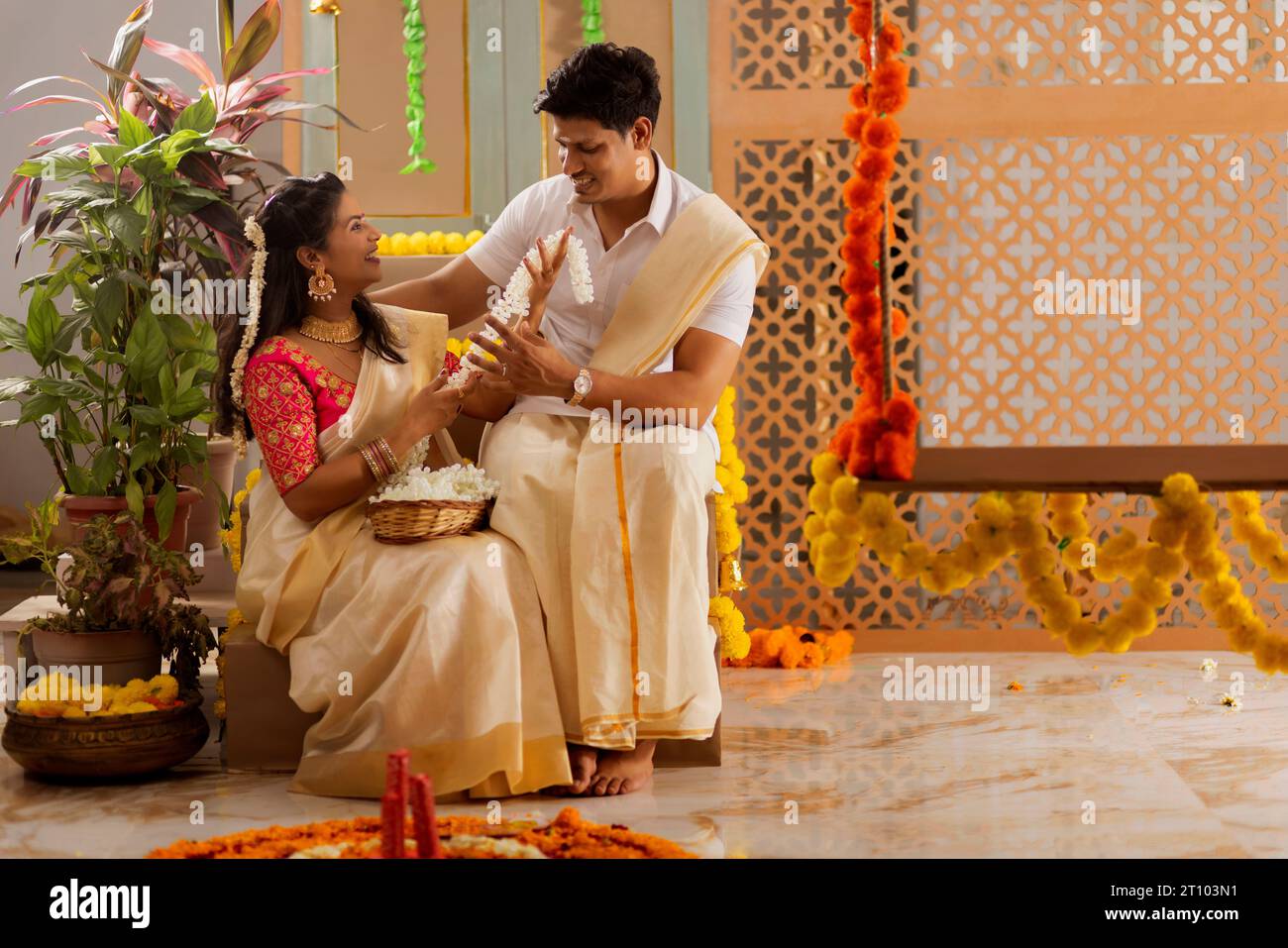 South Indian couple decorating house with flower garland to celebrate Onam Stock Photo