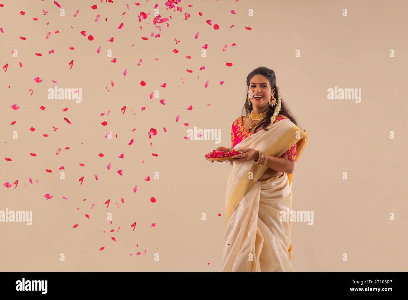 Smiling woman in traditional clothing holding a plate of rose petals against pain background Stock Photo