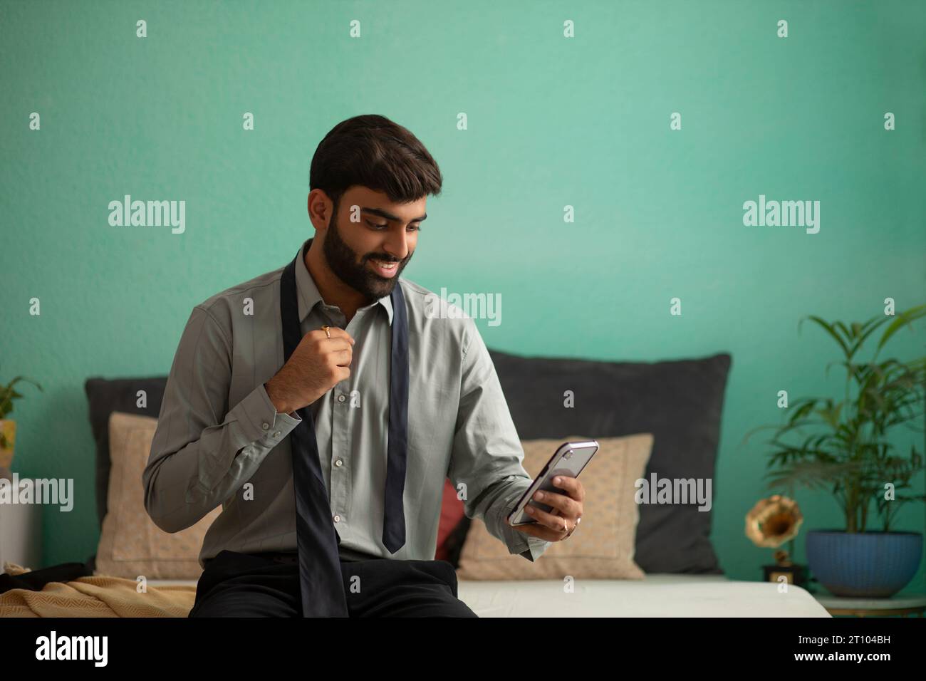 Young man using mobile phone while getting dressed Stock Photo