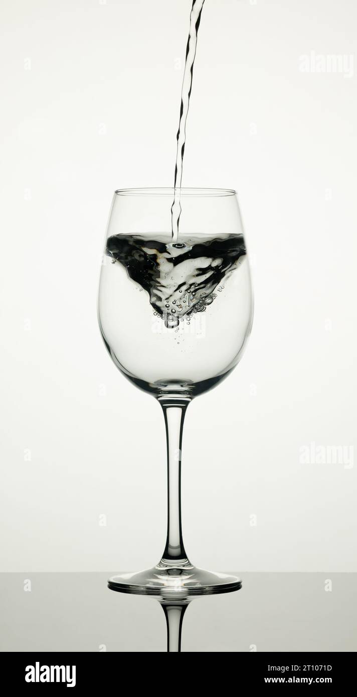 A glass of water on a white background with a stream falling and forming a swirl. Stock Photo