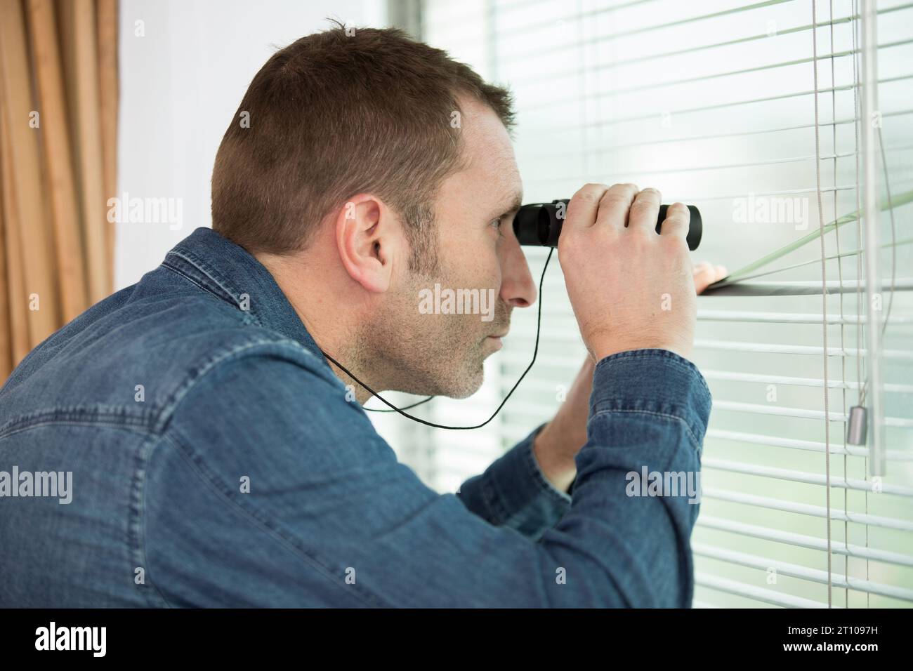 man watching out the window with binoculars Stock Photo