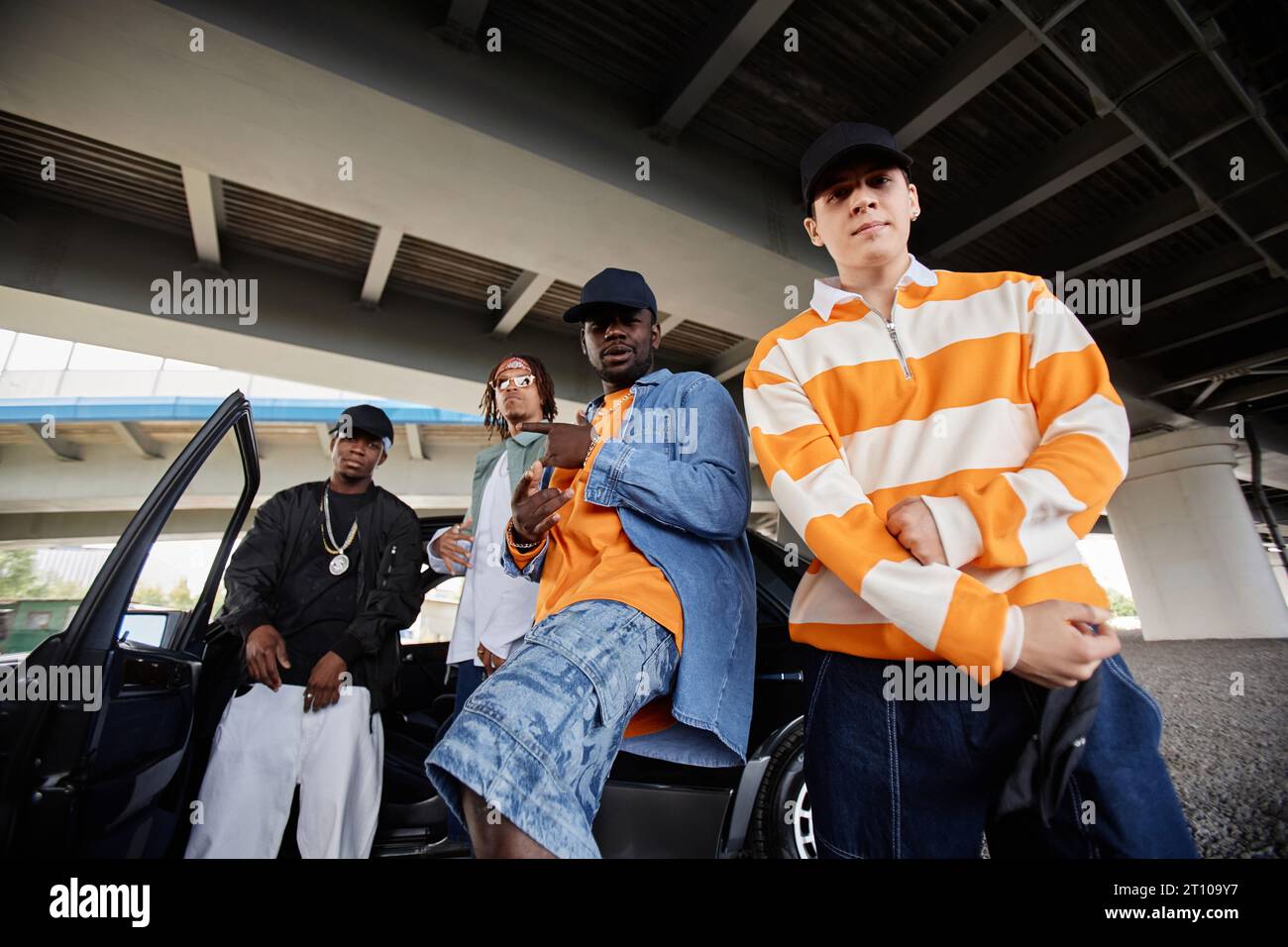 Three young intercultural hip hop dancers in casualwear standing by car under bridge in urban environment and performing new dance Stock Photo