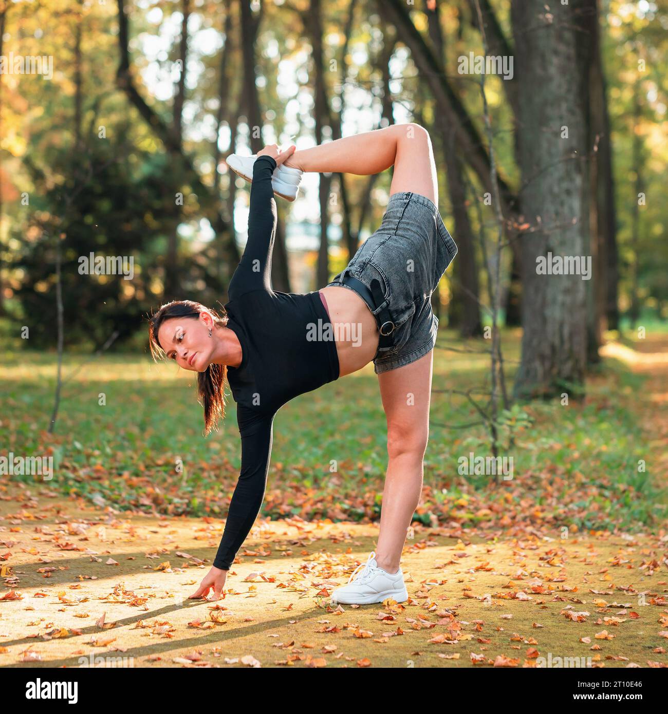 A woman practicing yoga performs a variation of the Ardha Chandrasana exercise, crescent pose, training while standing on a sunny warm autumn day in t Stock Photo