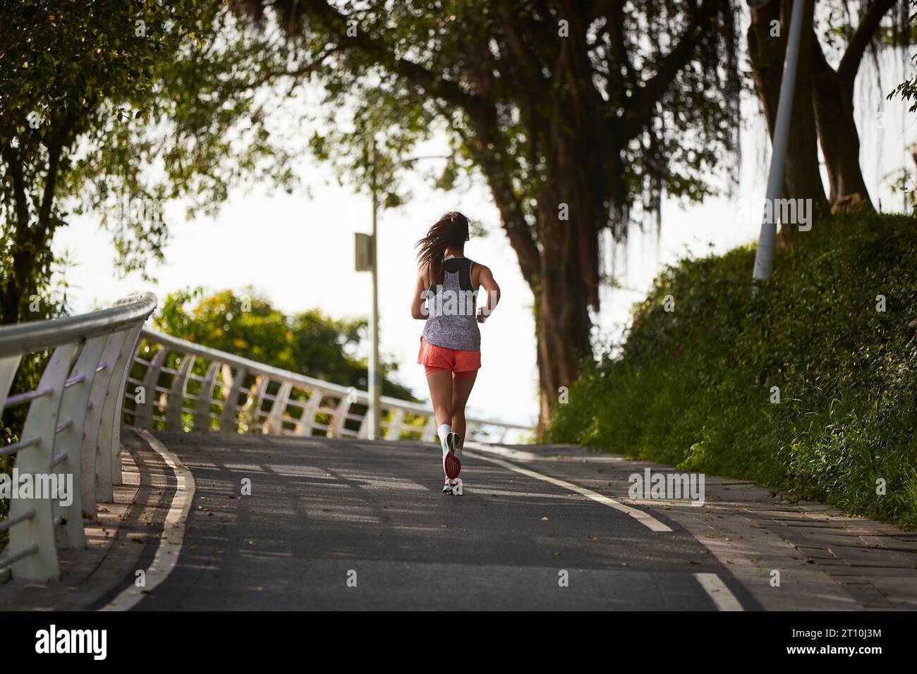 rear view of young asian woman female jogger exercising outdoors in city park Stock Photo