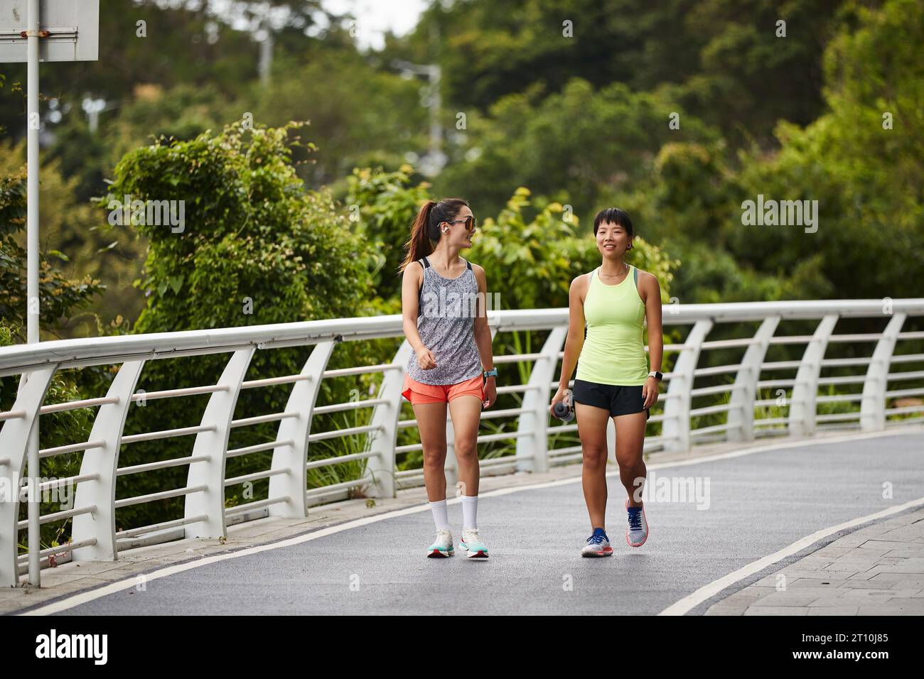 two young asian female joggers talking chatting while walking outdoors in city park Stock Photo