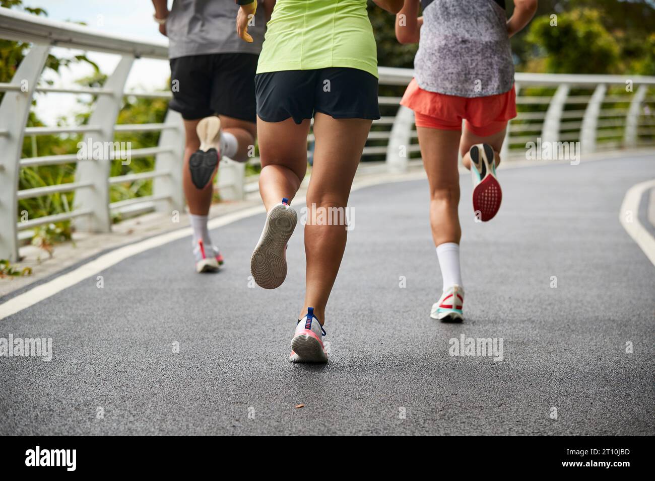 three young asian women female joggers exercising outdoors together in city park Stock Photo