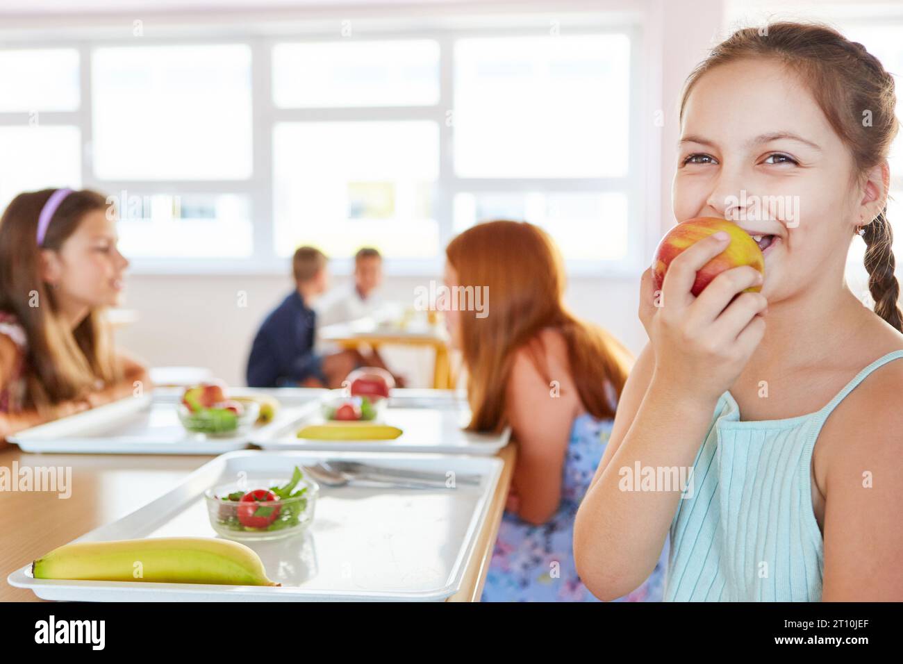 https://c8.alamy.com/comp/2T10JEF/happy-schoolgirl-eating-apple-while-sitting-with-friends-at-table-in-school-cafeteria-2T10JEF.jpg