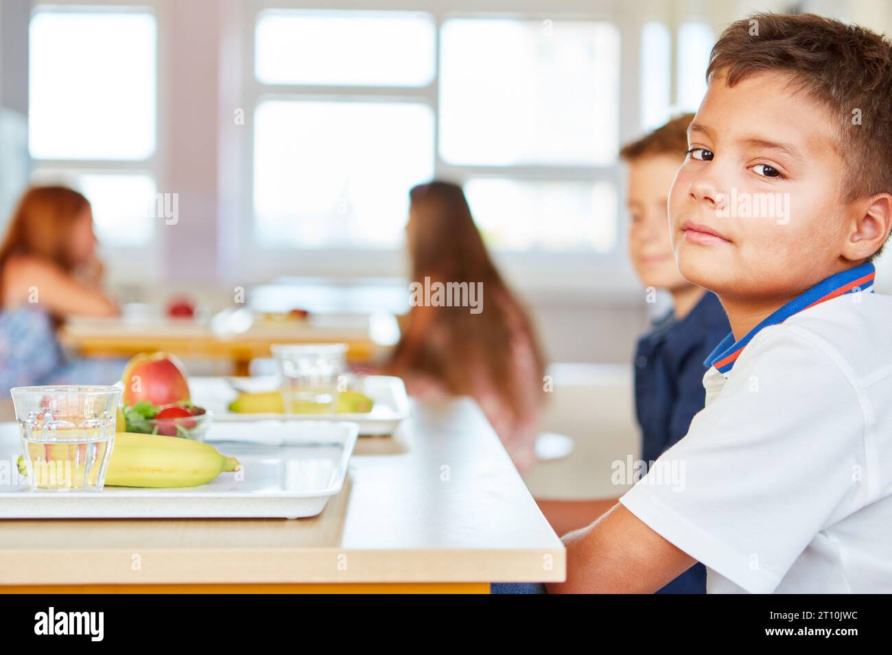 Side view portrait of boy sitting with fruits tray on table at cafeteria in school Stock Photo