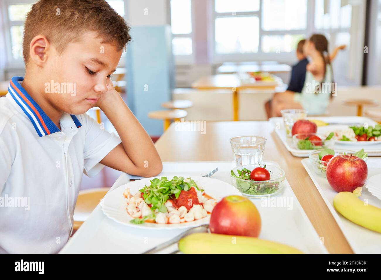 Sad schoolboy looking at food plate while sitting in school cafeteria Stock Photo