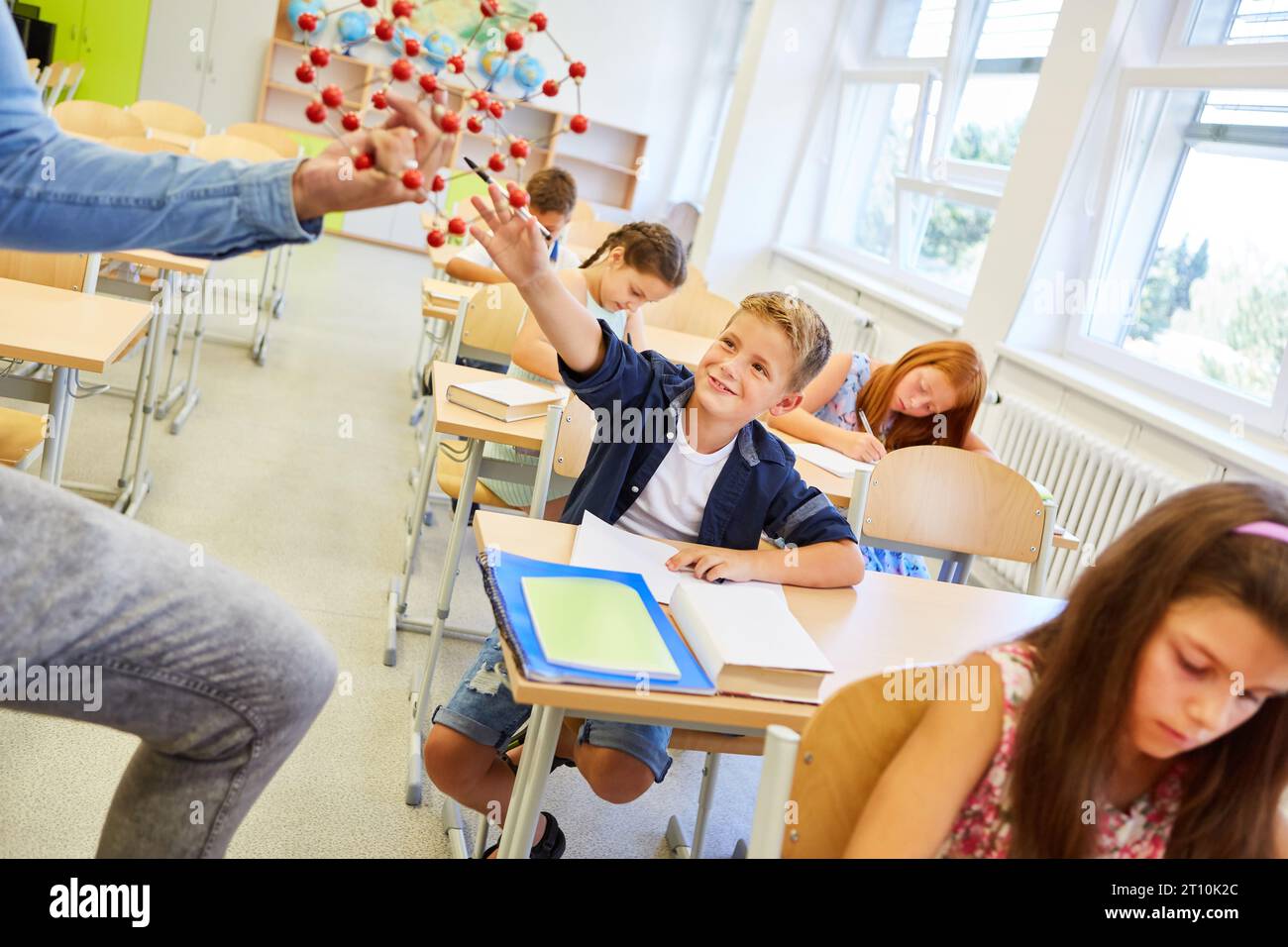 Smiling schoolkid touching molecular structure sitting on bench in classroom Stock Photo
