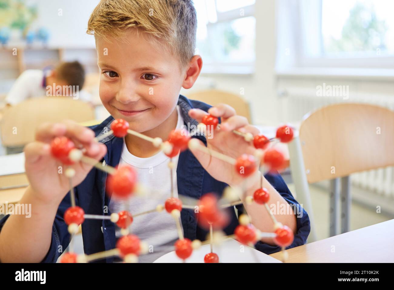 Smiling elementary schoolkid learning through molecular structure in class Stock Photo