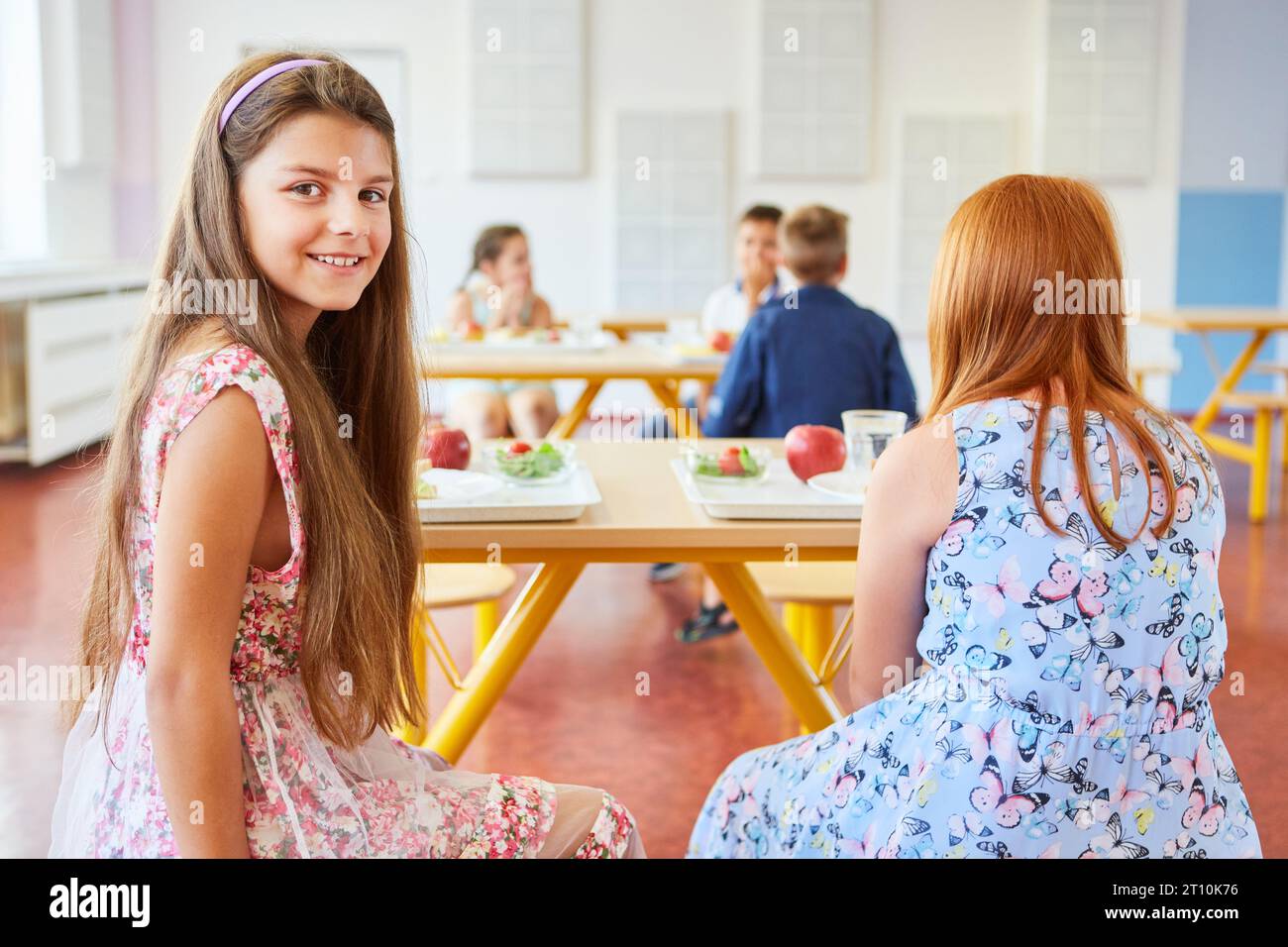 Portrait of smiling girl sitting with female friend in cafeteria at school Stock Photo