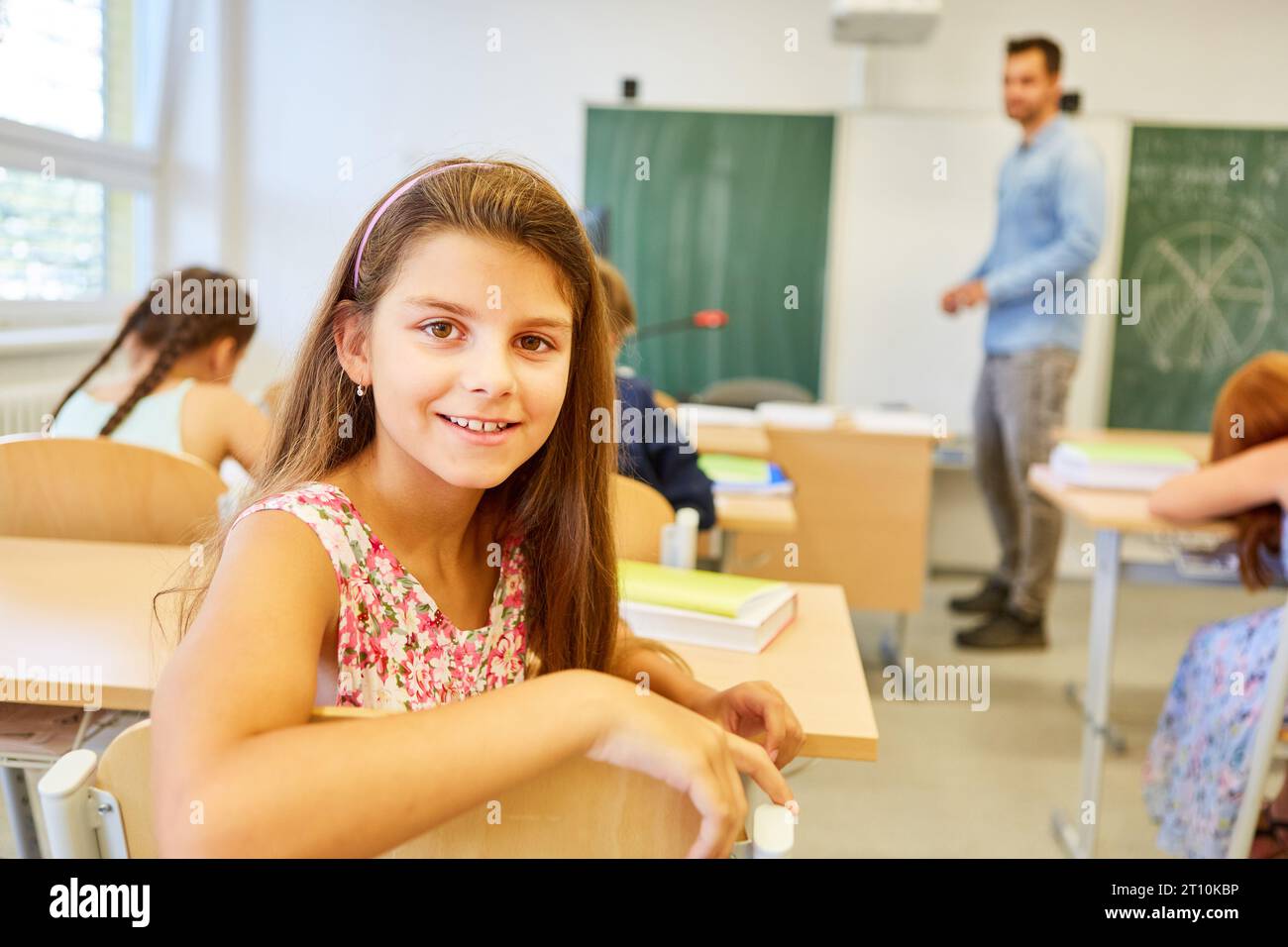 Portrait of smiling schoolgirl sitting on chair in classroom Stock ...